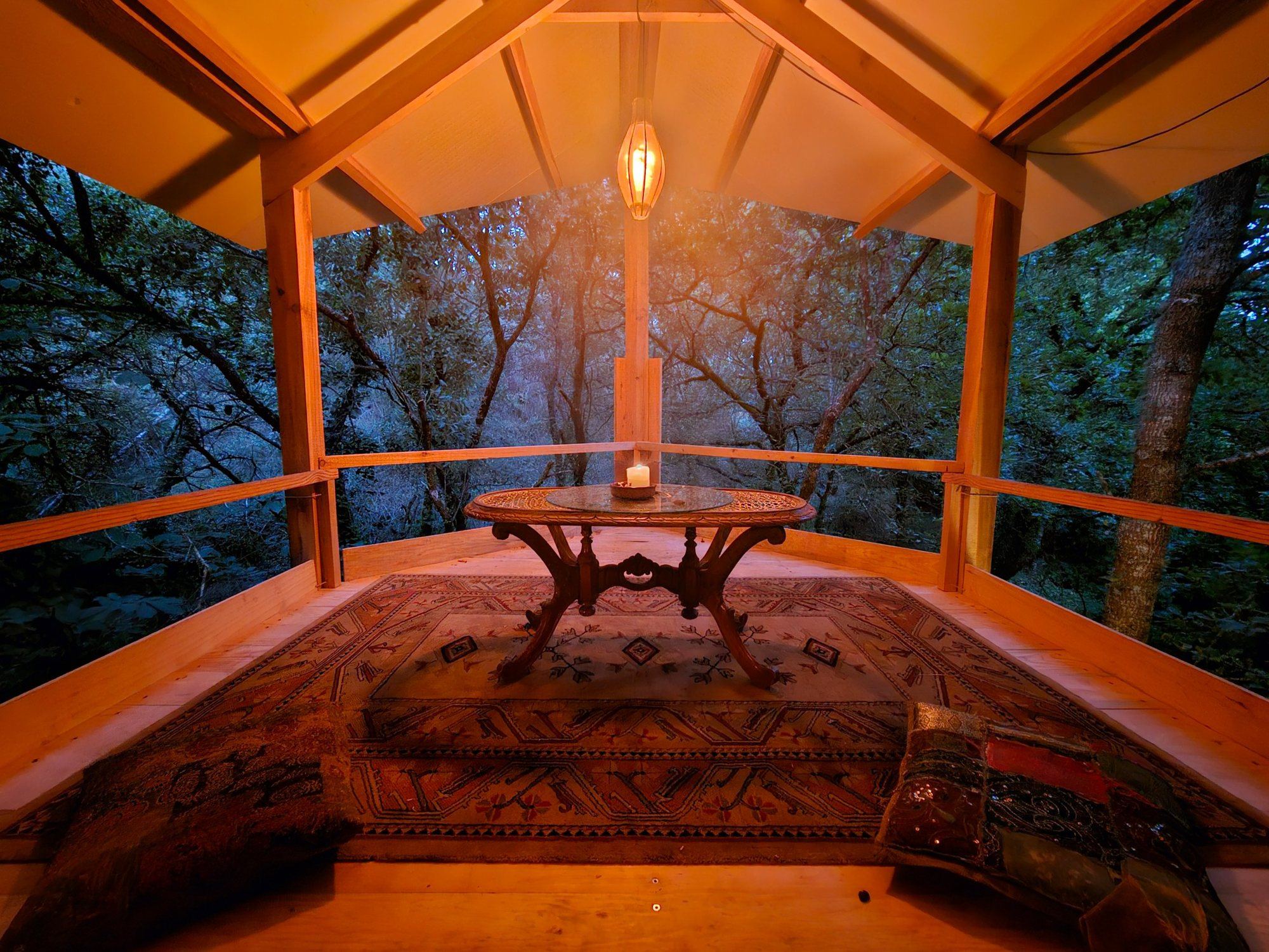 The Perch, a covered deck in the oak canopy, lit by a lantern at dusk