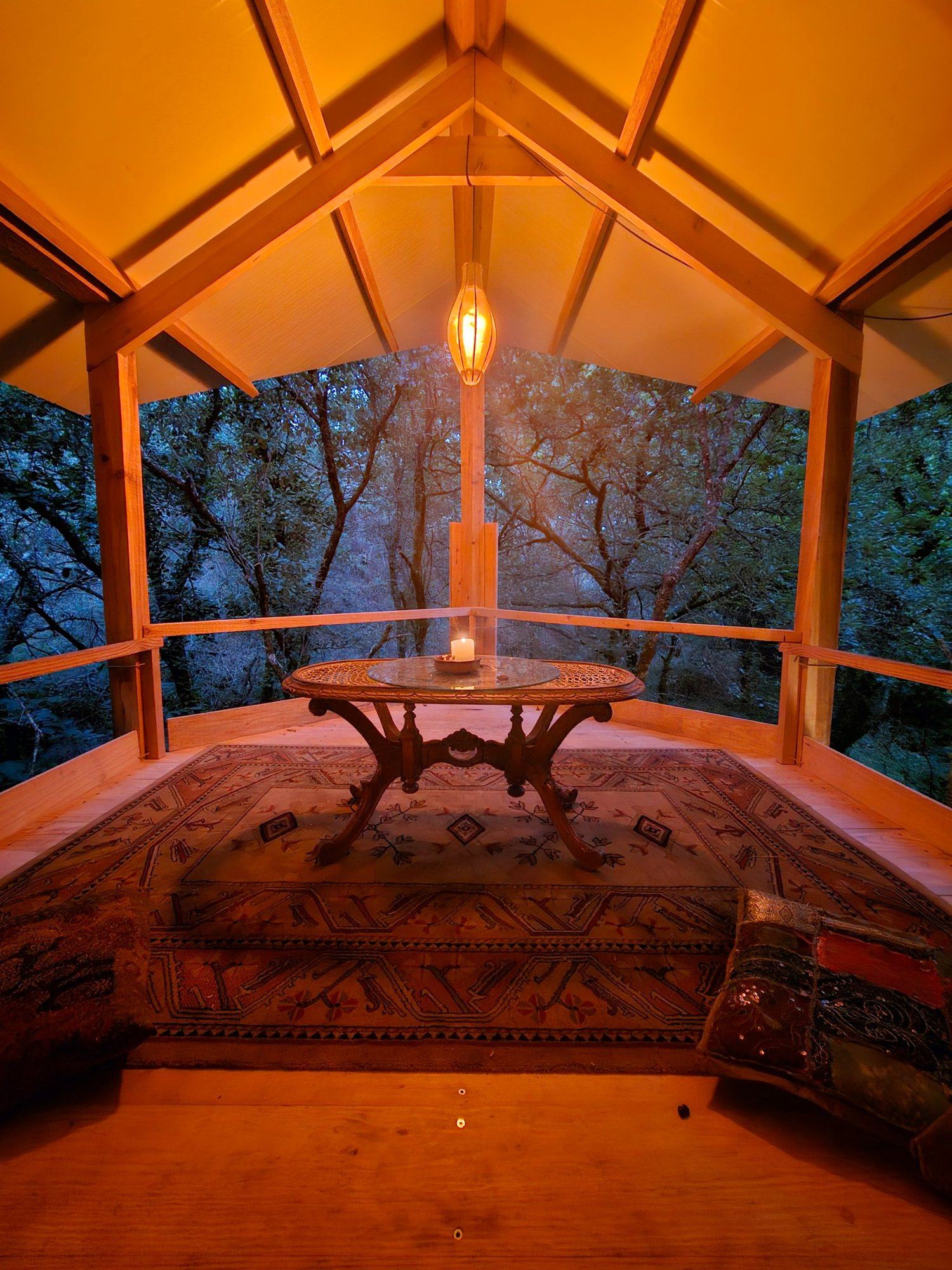 The Perch at dusk: a lantern, a candle on a carved table, a rug and cushions in the canopy